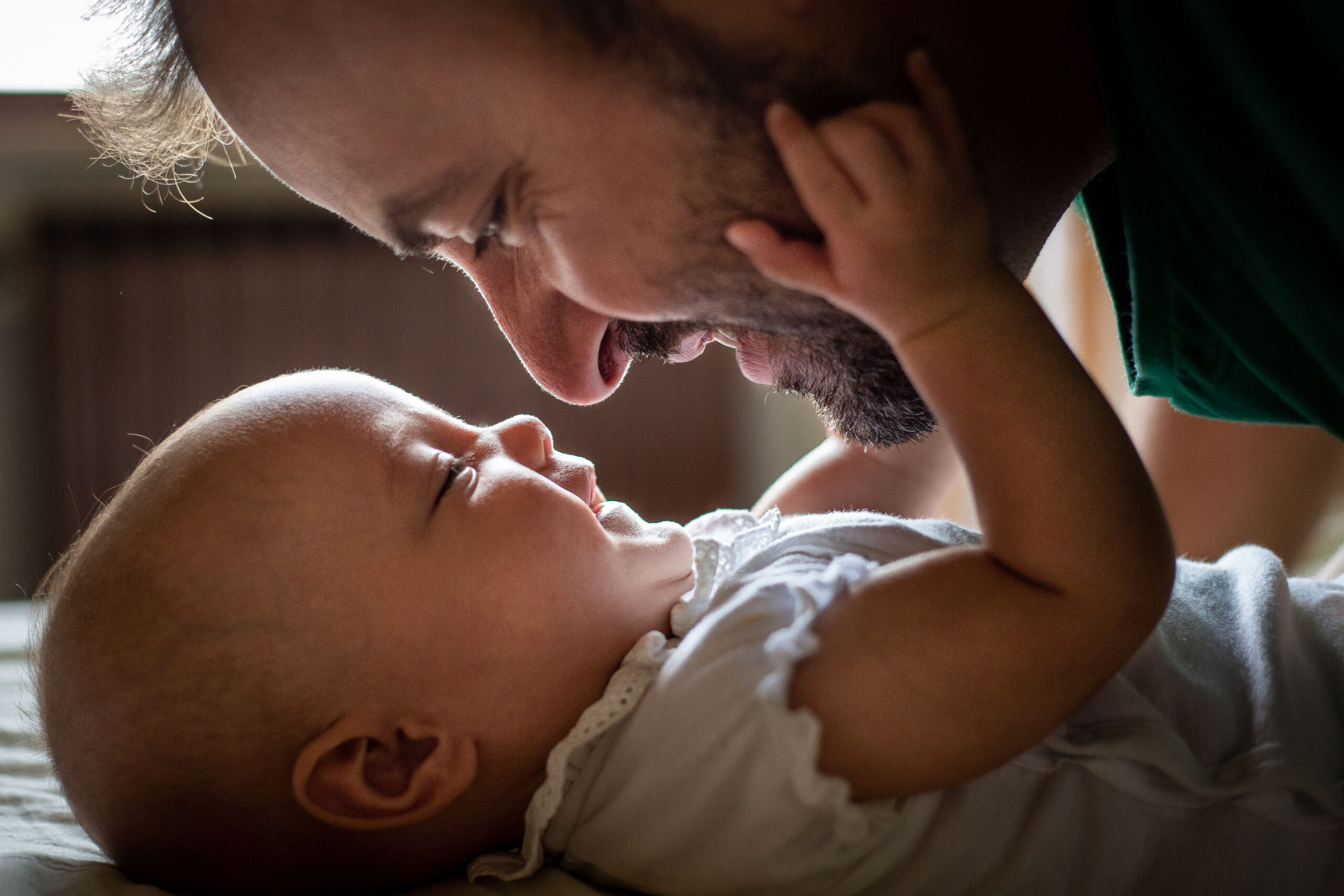 side view of father face watching his newborn baby in white top laying on the bed